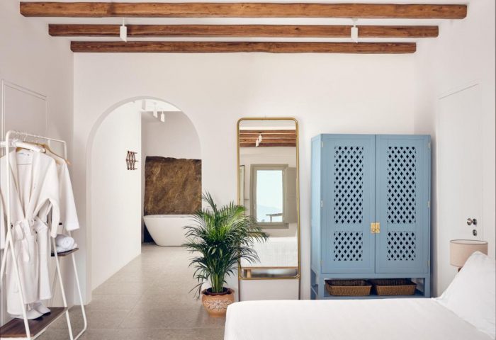 Belvedere Mykonos Hilltop Complex room. Gay-friendly hotel interior with white walls, blue cabinet, and arched doorway to bathroom.