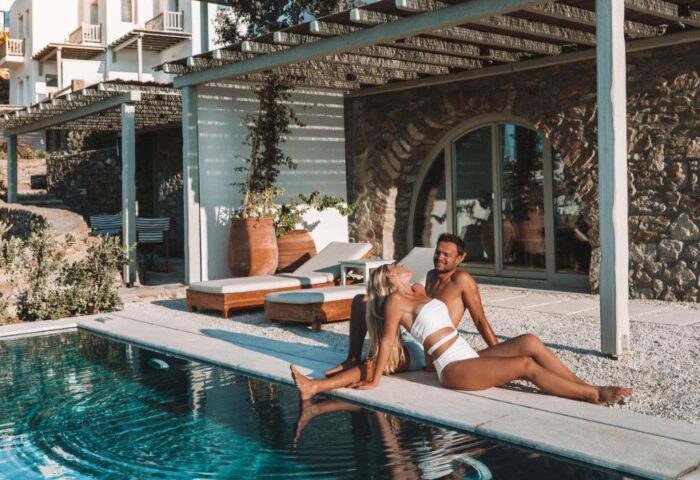Couple relaxing poolside at gay-friendly Belvedere Mykonos Hilltop Complex. Luxury travel destination with stunning architecture.
