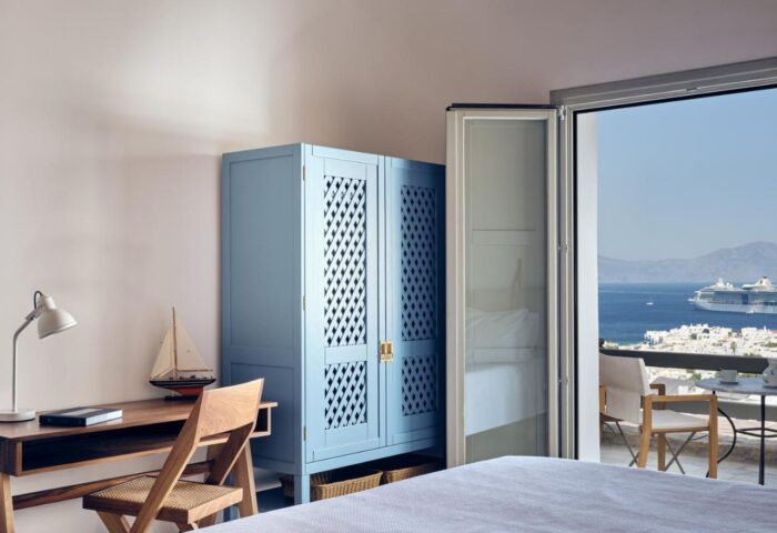 Belvedere Mykonos Hilltop Complex room. Gay-friendly hotel view: desk, blue closet, balcony, and cruise ship. Mykonos travel advice.