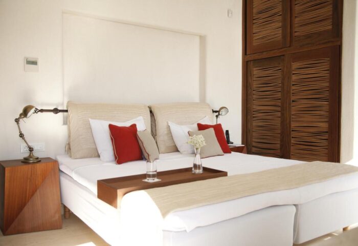 Belvedere Mykonos Waterfront Villa & Suites bedroom. Gay-friendly hotel room with bed, pillows, bedside table, and wooden closet.