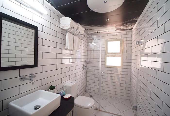 Ben Yehuda Apartments' bathroom. Modern design with white brick tiles, glass shower, sink, and toilet. Gay-friendly hotel for travel advice.