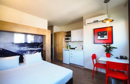 Ben Yehuda Apartments interior. Gay-friendly hotel room with bed, kitchenette, table, and chairs. Modern design for gay men's travel.