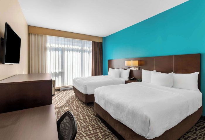 Best Western Plus Hotel Montreal guest room with two beds. Gay-friendly hotel room interior with desk, tv, and blue accent wall.