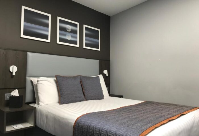 Bedroom in Best Western Plus Vauxhall Hotel, a gay-friendly hotel. Bed with gray headboard, pillows, and throw. Modern art on the dark wall.
