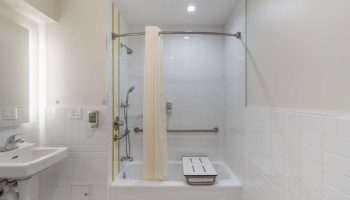 Best Western Red Coach Inn gay-friendly hotel bathroom. Accessible tub with seat and handrails. White tile and shower curtain.