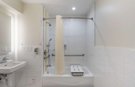 Best Western Red Coach Inn gay-friendly hotel bathroom. Accessible tub with seat and handrails. White tile and shower curtain.