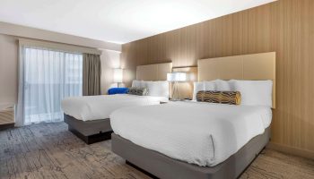 Best Western Red Coach Inn gay-friendly hotel room. Two beds with white linens and patterned pillows. Balcony with sheer curtains. Lamps on nightstands.