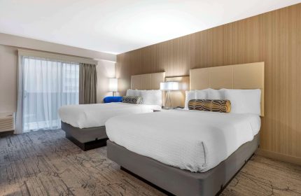 Best Western Red Coach Inn gay-friendly hotel room. Two beds with white linens and patterned pillows. Balcony with sheer curtains. Lamps on nightstands.