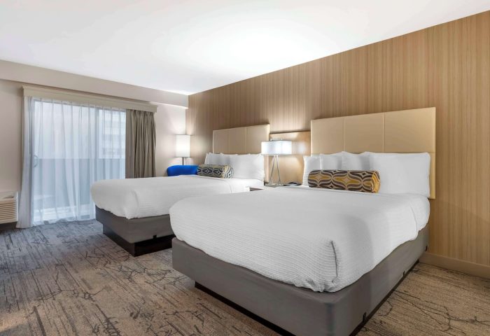 Best Western Red Coach Inn gay-friendly hotel room. Two beds with white linens and patterned pillows. Balcony with sheer curtains. Lamps on nightstands.