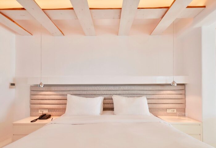 Bill & Coo Suites and Lounge bedroom. Gay-friendly hotel room with white linens, headboard, and wood beam ceiling. Luxury travel for gay men.