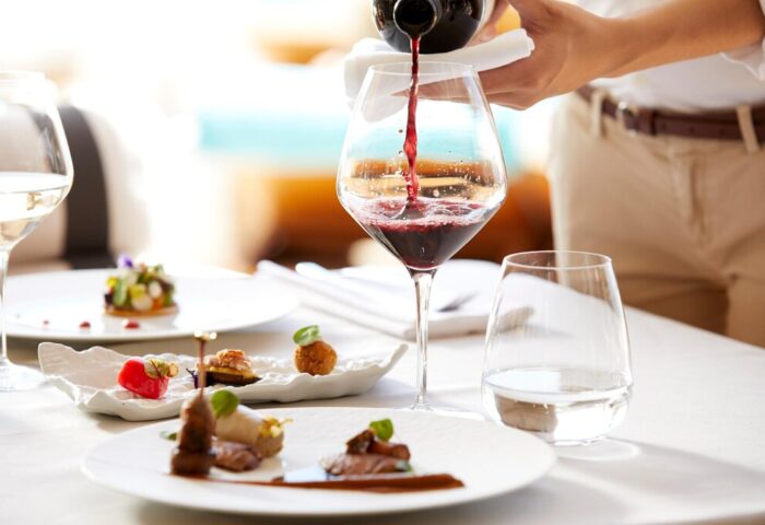Fine dining at Bill & Coo Suites, a gay-friendly hotel. Red wine is poured. Exquisite dishes on white plates. Luxury travel.