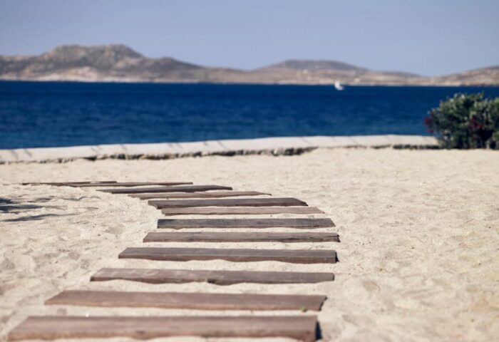 Wooden path on the beach at Bill & Coo Suites and Lounge, a gay-friendly hotel. Ocean view in Mykonos, Greece.