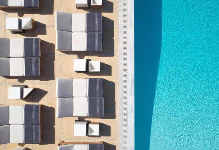 Aerial view of Bill & Coo Suites and Lounge's pool area. Gay-friendly hotel with stylish sunbeds and crystal-clear water. Mykonos luxury.