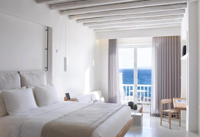 Bill & Coo Suites and Lounge gay-friendly hotel room. White interior, bed, balcony with sea view. Luxury gay travel destination.