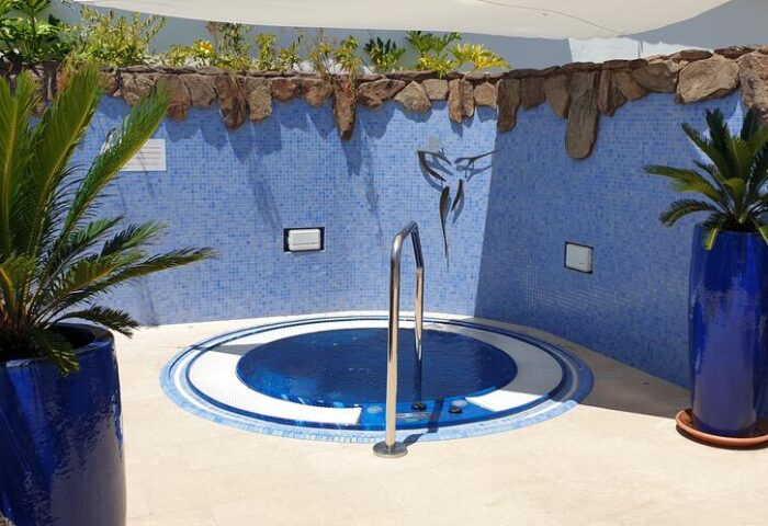 Birdcage Gay Men Resort hot tub. Gay-friendly hotel's outdoor jacuzzi with blue mosaic tiles, plants, and a stainless steel handrail.