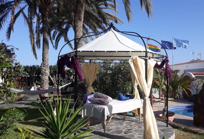 Birdcage Gay Men's Resort: Outdoor massage gazebo with rainbow flag. Gay-friendly hotel for gay men's travel and lifestyle. Palm trees.