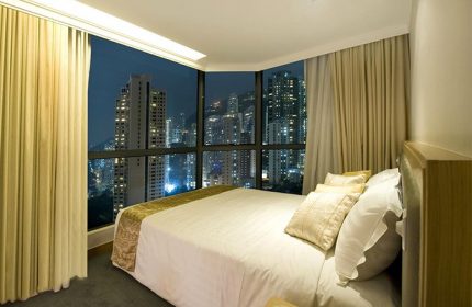 Bedroom at Bishop Lei International House, a gay-friendly hotel in Hong Kong, with a city view at night. Hotel room interior.