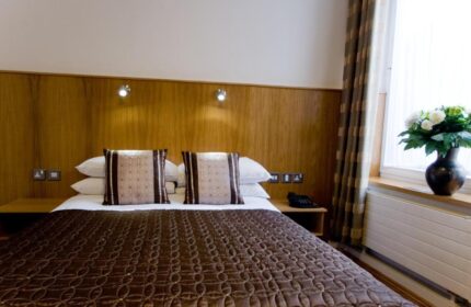 Blooms Hotel bedroom. Gay-friendly hotel room with a double bed, brown patterned quilt, pillows, bedside tables, and a vase of flowers by the window.