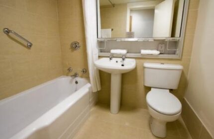 Blooms Hotel gay-friendly bathroom. Bathtub, sink, and toilet in a clean, well-lit space. Ideal for gay men's travel, ensuring comfort and convenience.