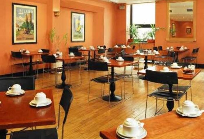 Blooms Hotel's dining area, a gay-friendly hotel. Tables with teacups fill the room. A mirror and art adorn the walls in this Dublin hotel.