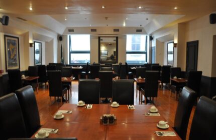 Blooms Hotel's dining room. Gay-friendly hotel with set tables, black chairs, and wooden floors. Ideal for gay men travel in a welcoming space.