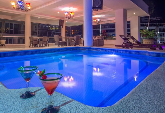 Blue Chairs Resort by the Sea Adults Only pool at night with cocktails. Gay-friendly hotel with bar, lounge chairs, and colorful lighting.