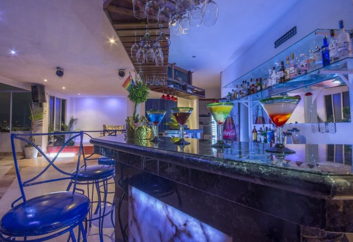Bar at Blue Chairs Resort by the Sea, adults-only gay-friendly hotel. Cocktails on the bar, blue chairs, and rainbow flag. Gay travel.