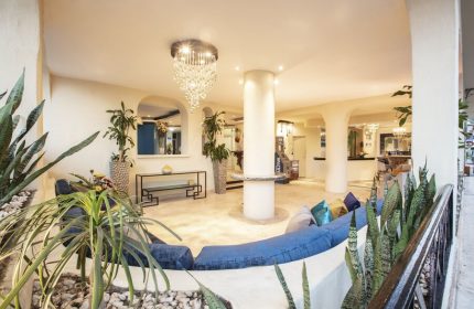 Lobby at Blue Chairs Resort by the Sea, a gay-friendly, adults-only hotel. Blue couch, chandelier, plants. Gay travel in Puerto Vallarta.