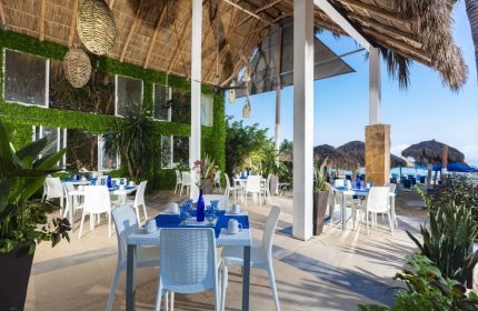 Blue Chairs Resort by the Sea adults-only gay-friendly hotel restaurant. Tables with blue decor, beach view, and thatched roof.