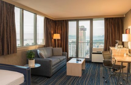 Blue Horizon Hotel suite interior. Gay-friendly hotel room with city view, sofa, desk, and blue wave patterned carpet. Modern design for gay men travel.