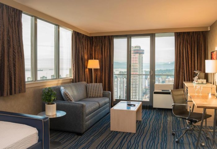 Blue Horizon Hotel suite interior. Gay-friendly hotel room with city view, sofa, desk, and blue wave patterned carpet. Modern design for gay men travel.