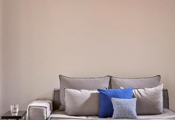 Boheme Mykonos Hotel adults-only room. Modern gray sofa with blue pillows, wooden table, and rope light fixture. Gay-friendly hotel.