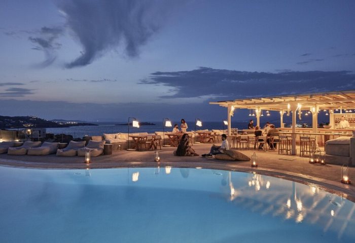 Boheme Mykonos Hotel adults-only, gay-friendly. Poolside bar at dusk with guests enjoying drinks and the ocean view. Mykonos nightlife.