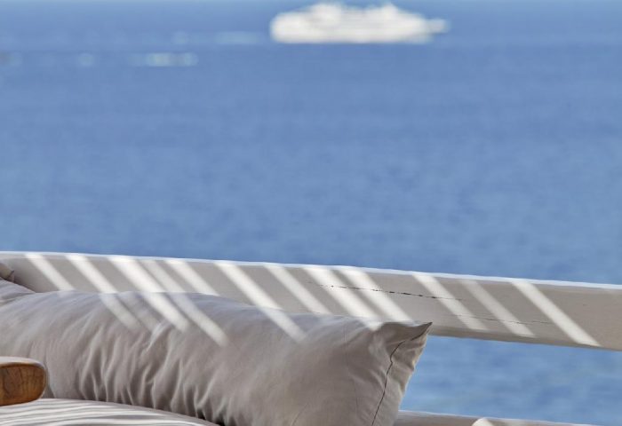 Boheme Mykonos Hotel adults-only detail. Hat and sunglasses on a Mykonos balcony overlooking the sea. Gay-friendly hotel travel.