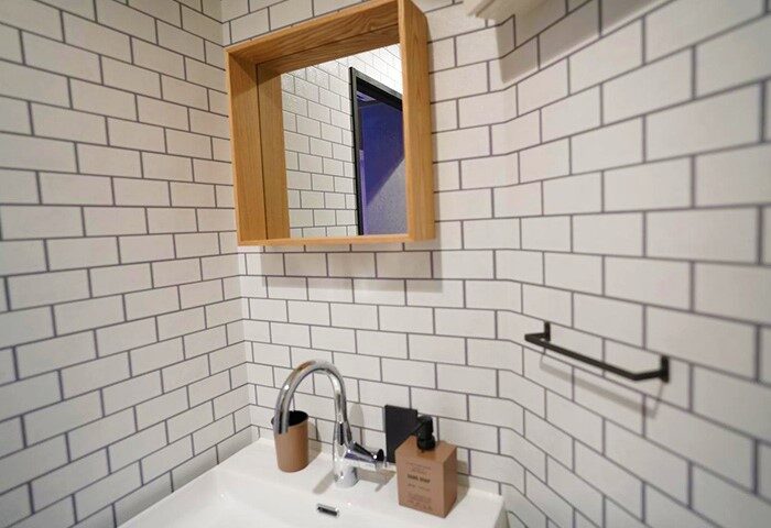 Bathroom at Book Tea Bed SHINJUKU-GYOEN, a gay-friendly hotel. Sink, mirror, white tile walls. Modern design for gay travelers in Tokyo.