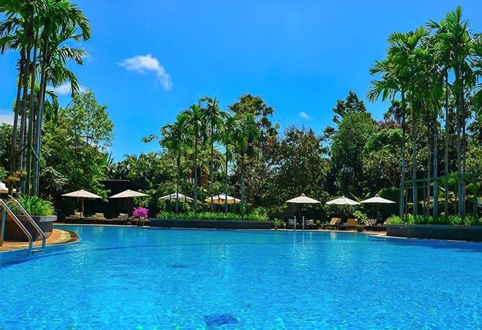 Borei Angkor Resort & Spa pool view. Gay-friendly hotel in Siem Reap, Cambodia. Relaxing vacation for gay men. Palm trees, blue sky.