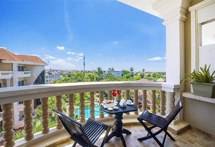 Balcony view at Borei Angkor Resort & Spa, a gay-friendly hotel. Table set for two overlooking pool and Siem Reap, Cambodia. Relaxing travel.