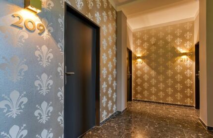 Hallway at Boutique Hotel 026 Köln St. Michael, a gay-friendly hotel. Room doors with fleur-de-lis wallpaper and modern lighting. Stylish decor.
