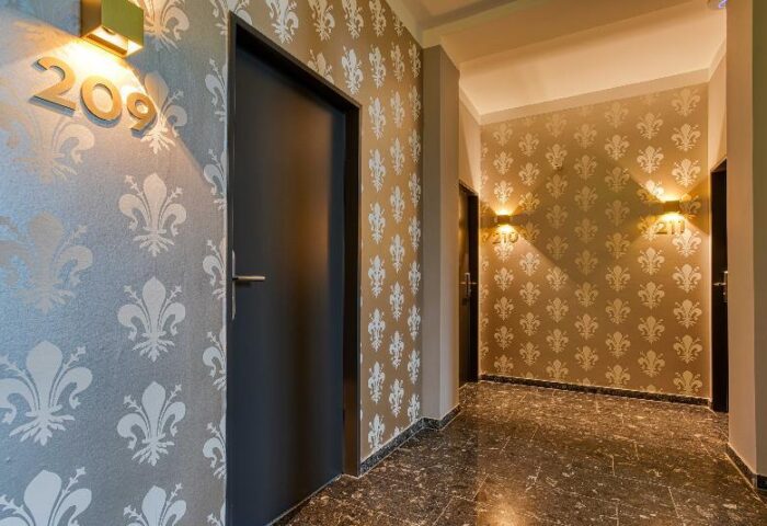 Hallway at Boutique Hotel 026 Köln St. Michael, a gay-friendly hotel. Room doors with fleur-de-lis wallpaper and modern lighting. Stylish decor.