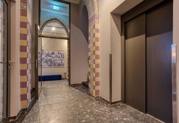 Boutique Hotel 026 Köln St. Michael interior. Hallway view with elevator and arched doorway. Gay-friendly hotel with unique design elements.