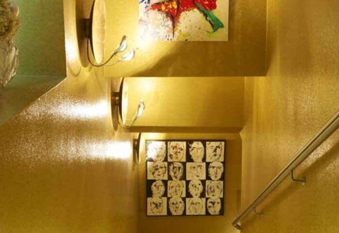 Stairwell at Boutiquehotel Das Tyrol, a gay-friendly hotel. Gold walls, modern art, & unique lighting create a stylish, welcoming vibe.