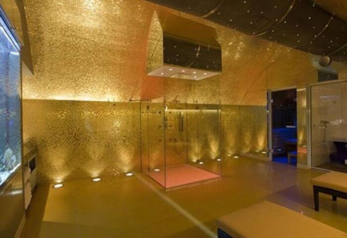Boutiquehotel Das Tyrol's gay-friendly luxury bathroom. Features a gold mosaic wall, glass shower, and sleek design. Ideal for gay men travel.