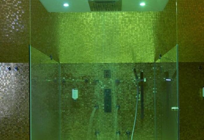 Shower in Boutiquehotel Das Tyrol, a gay-friendly hotel. The shower has gold mosaic tiles and glass doors. Great for gay travel.