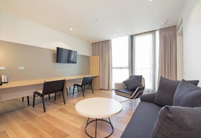 Brady Hotels Central Melbourne gay-friendly hotel room. Modern interior with sofa, chairs, desk, and TV. Comfortable and stylish accommodation.