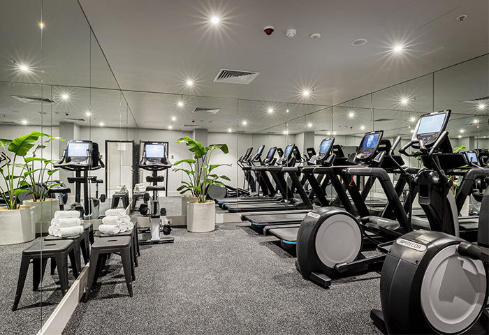 Brady Hotels Jones Lane gym. Gay-friendly hotel fitness center with treadmills, elliptical machines, stationary bikes, and towels. Plants add a touch of nature.