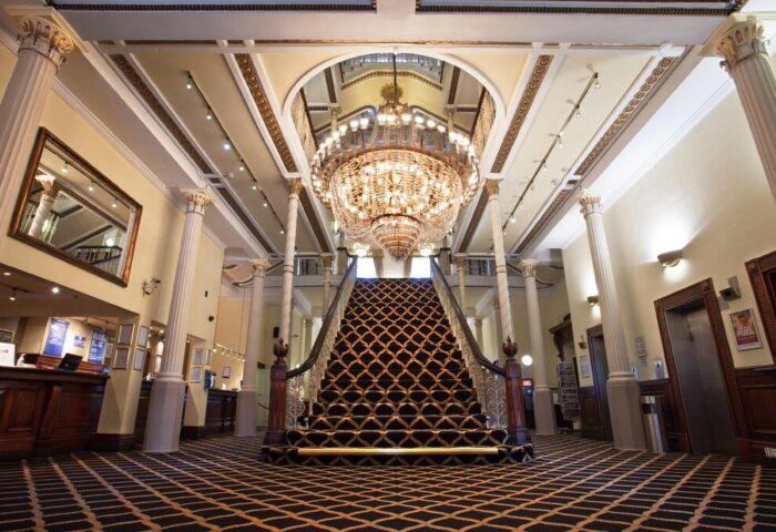 Britannia Manchester Hotel's grand lobby. Gay-friendly hotel with a large staircase, chandelier, and ornate architecture. Perfect for gay travel.