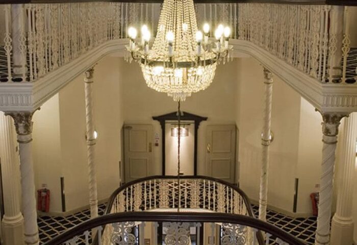 Britannia Manchester Hotel's grand staircase with ornate railings, columns, and a sparkling chandelier. Gay-friendly hotel architecture.