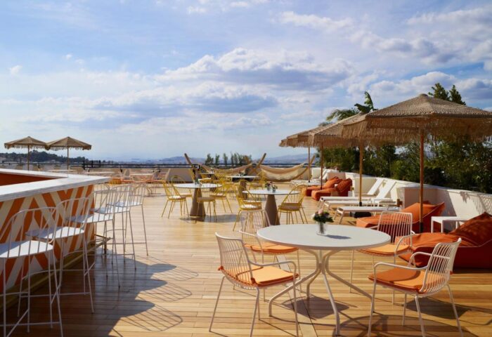 Brown Acropol Hotel rooftop bar, a gay-friendly spot in Athens. Tables, chairs, umbrellas, and lounge seating offer relaxation with city views.