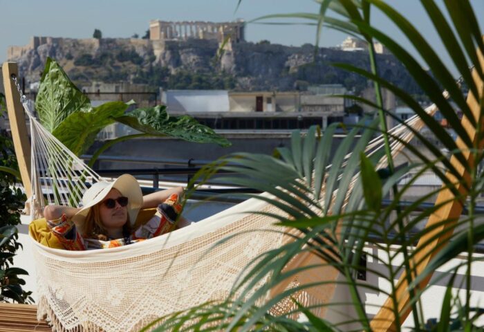 Brown Acropol, a gay-friendly hotel. Woman relaxing in a hammock with Acropolis view. Athens hotel rooftop experience.