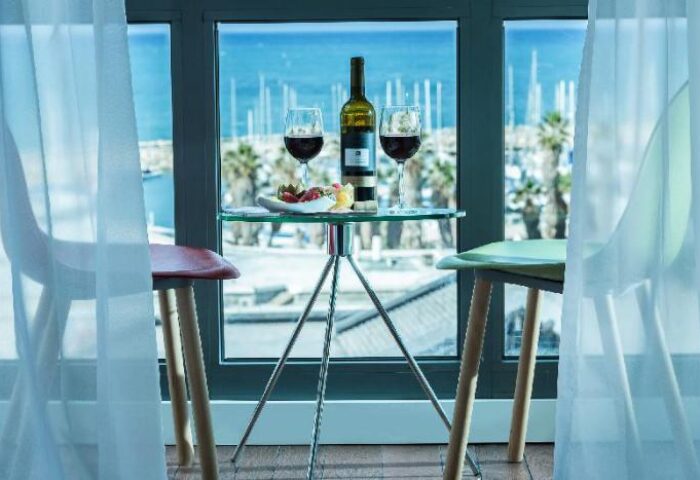 Brown Seaside Hotel view. Wine and fruit on a glass table, with a sea view. Gay-friendly hotel room, perfect for a romantic getaway.